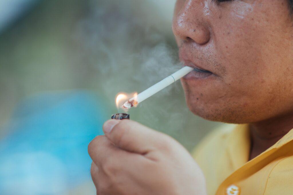 A close-up of a person lighting a cigarette, with visible smoke emanating from the lit end as it nears their mouth