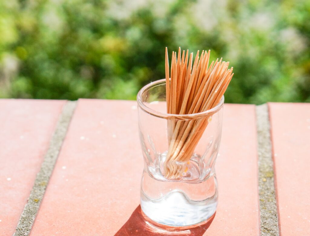 Glass full of wooden toothpicks on an outdoor table with natural greenery in the background, an alternative to dental floss.