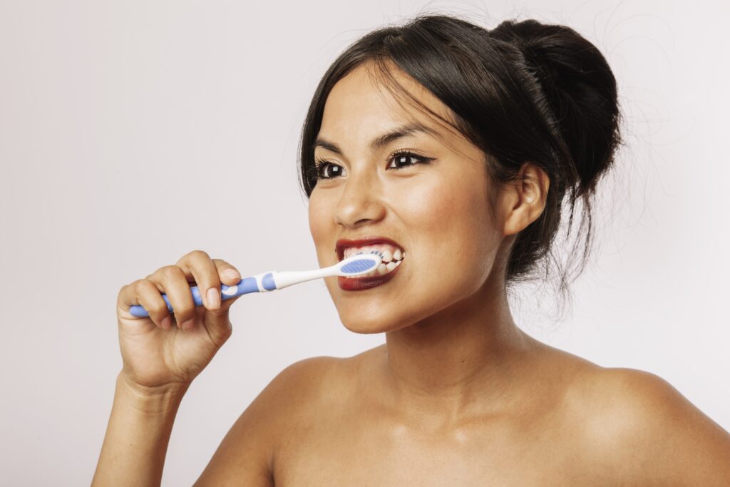 Smiling woman practicing proper teeth brushing technique with a manual toothbrush for oral health care.