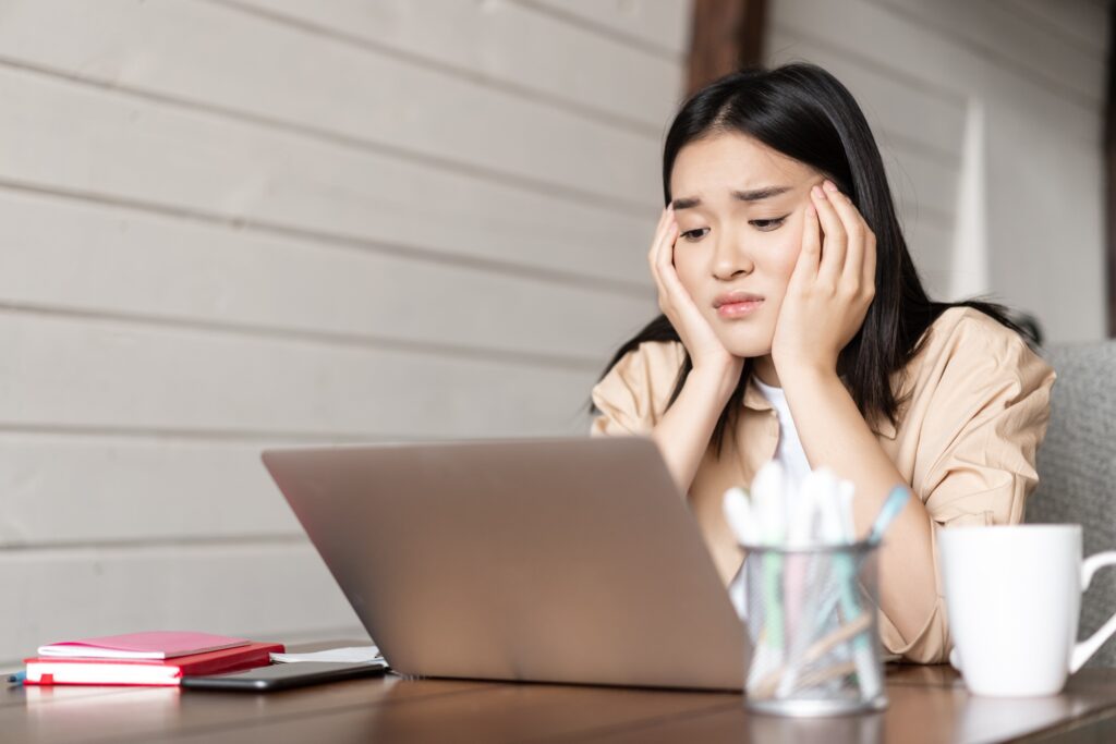A young Asian woman looking stressed and tired as she studies from her laptop, embodying the challenges of managing bruxism and stress.